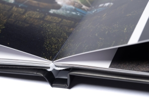 Close-up of an open photo album with glossy pages and a nature image showing greens and water, viewed at an angle; a white thread lies along the spine.