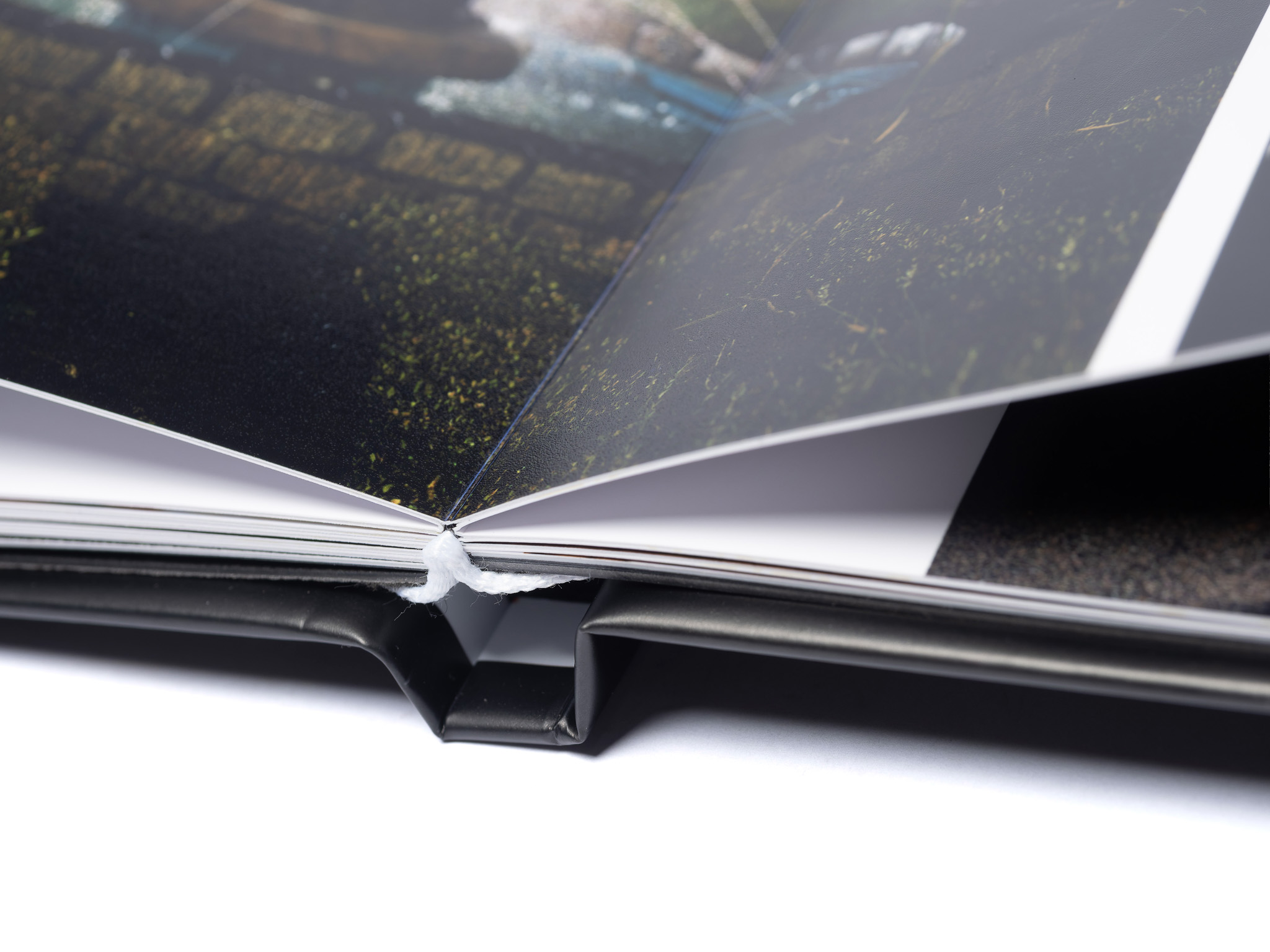 MemoryAlbum_04 | Weddings by Michael Close-up of an open photo album with glossy pages and a nature image showing greens and water, viewed at an angle; a white thread lies along the spine.